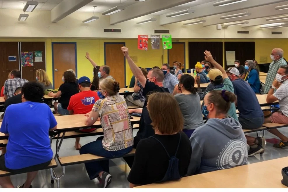 Families raising their hands at a PTA general meeting in the school cafeteria